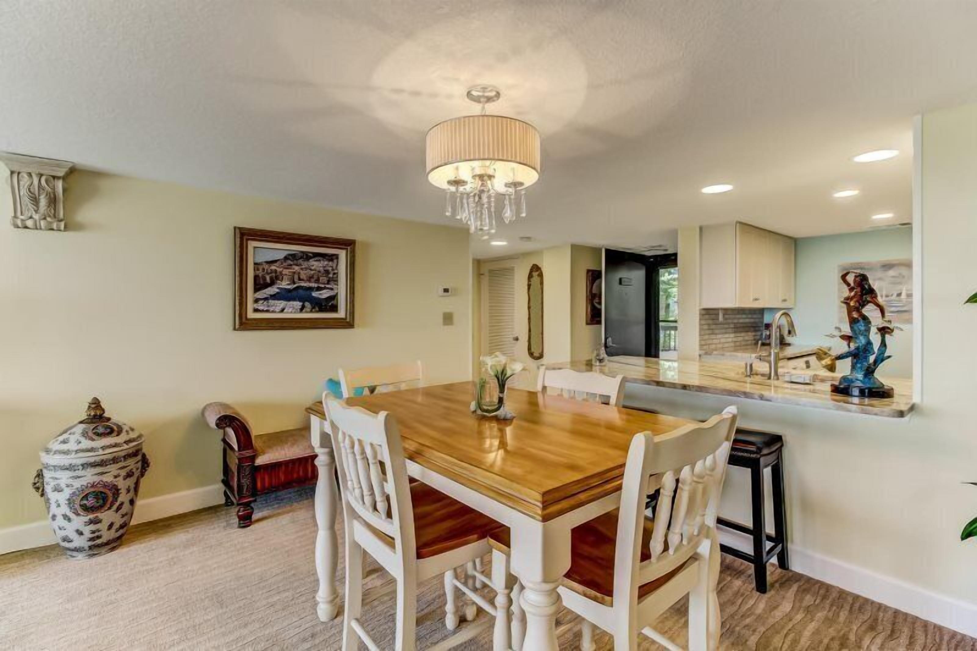A dining area with a wooden table and white chairs, a chandelier, and a vase with flowers.