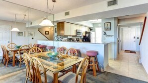 Un'ampia sala da pranzo con tavolo in vetro e sedie in legno, una cucina con elettrodomestici moderni e una scala a vista che conduce a un altro livello.