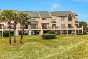 A multi-story hotel with a flat roof, balconies, and a well-maintained lawn with palm trees. - 209-sailmaker (Fernandina Beach)