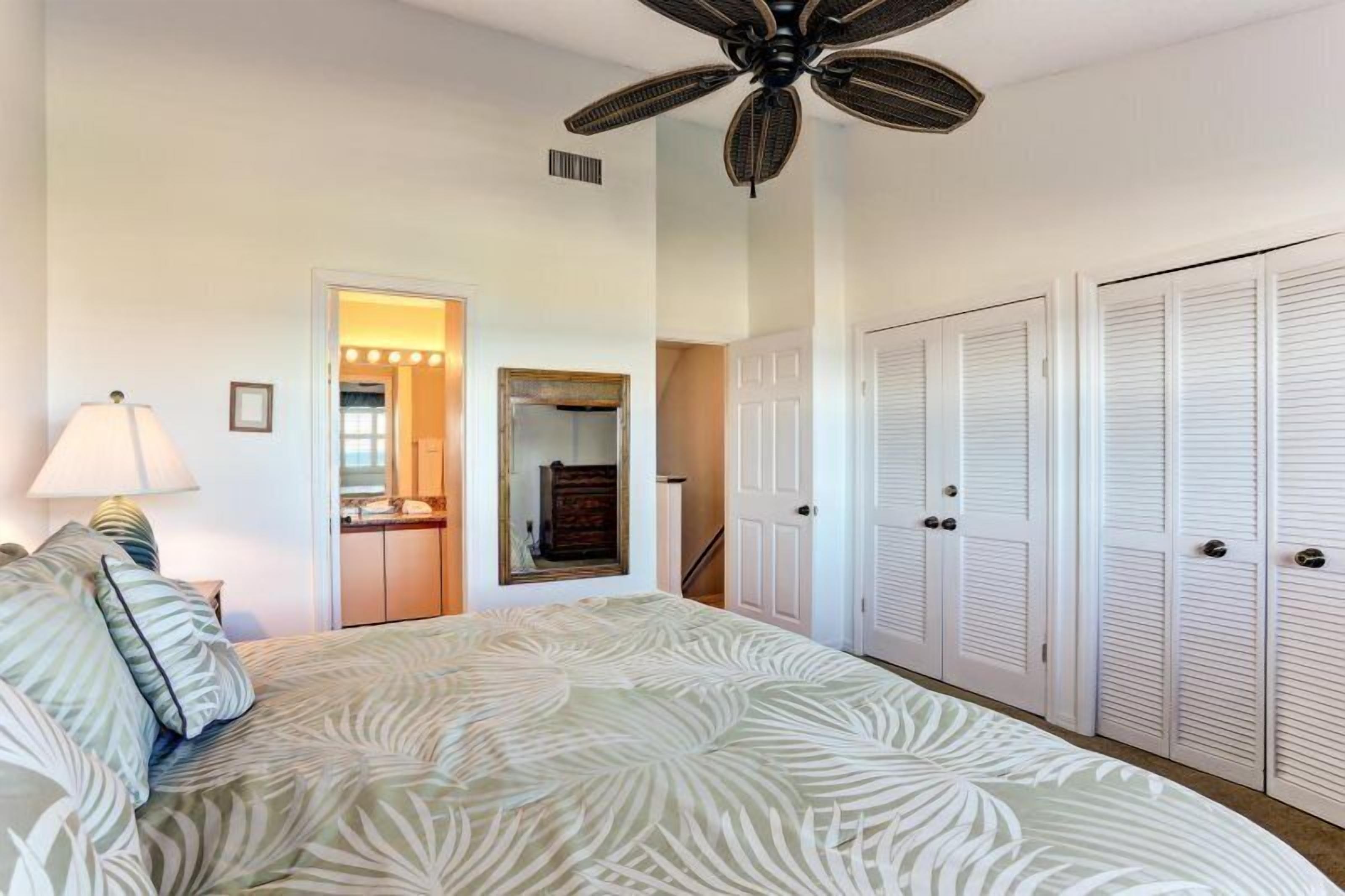A bedroom with a bed, a ceiling fan, a mirror, and a set of white closets.