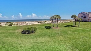 Una proprietà fronte spiaggia con un prato curato, palme e un'ampia casa con diverse finestre e un balcone.