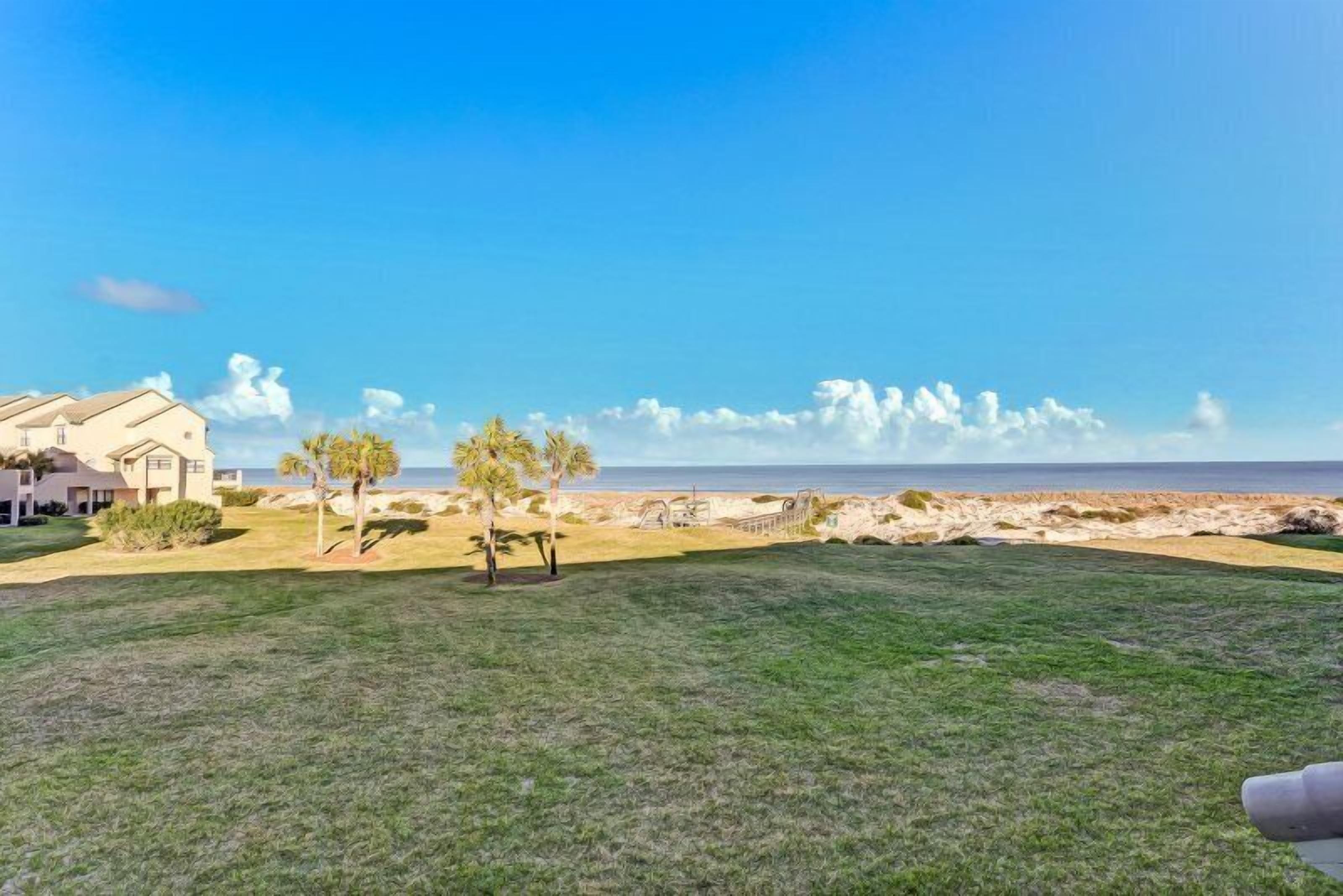A beachfront property with a grassy lawn, palm trees, and a view of the ocean.