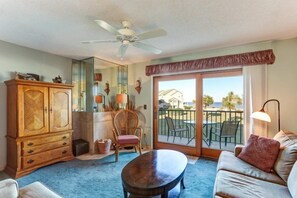 Relax in this stylish living room with a sofa, wicker chair, and floor lamp, leading to a patio with a view.