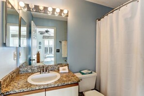 A bathroom with a granite countertop sink, a white toilet, and a shower curtain. - 209-sailmaker (Fernandina Beach)