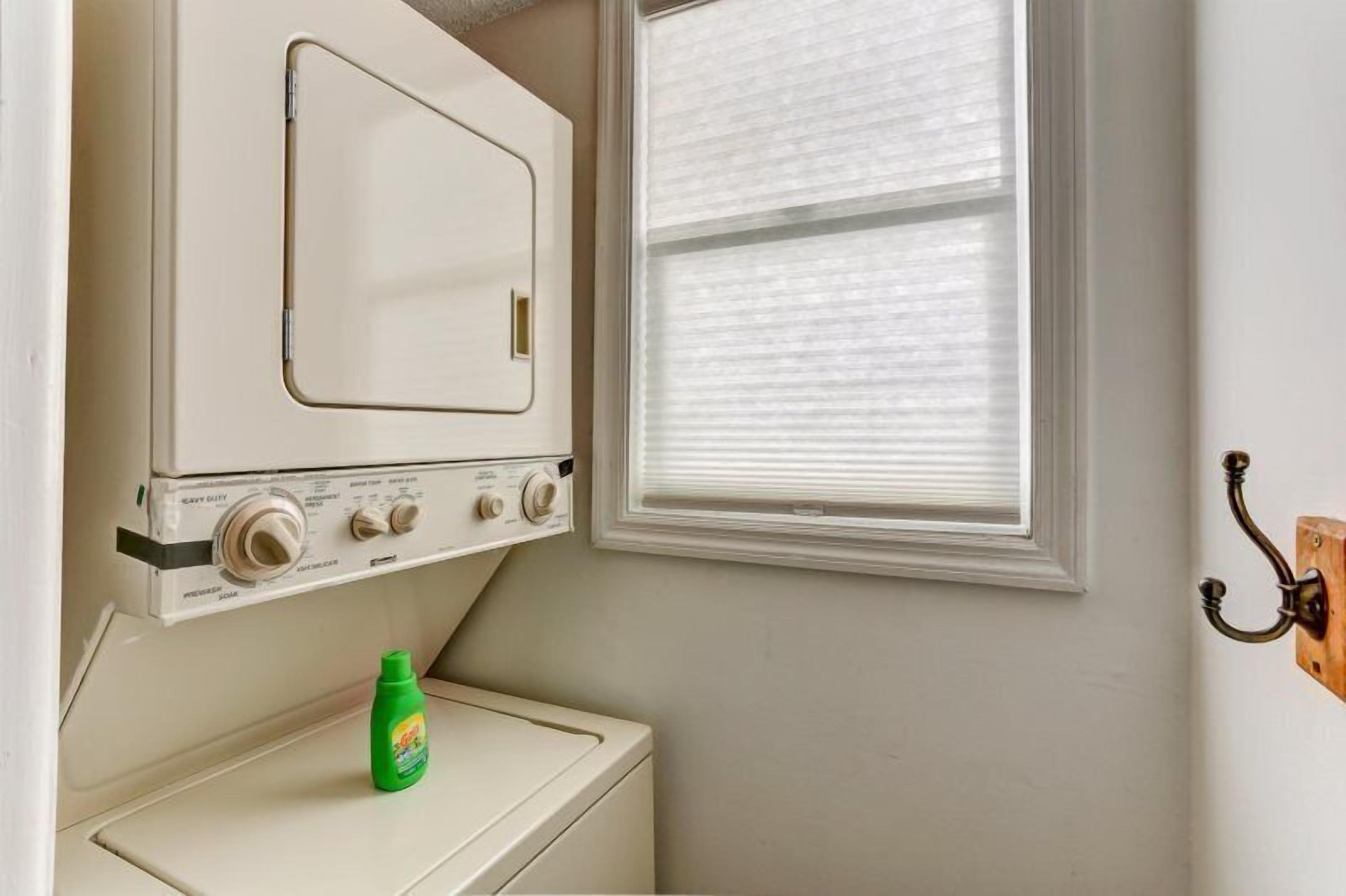A laundry area with a washing machine and dryer, a window with blinds, and a wall-mounted hook.