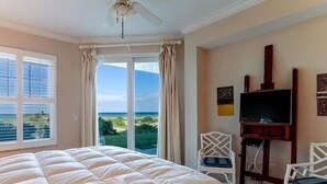 Een slaapkamer met een groot bed, een plafondventilator, een televisie en uitzicht op de oceaan door de ramen.
