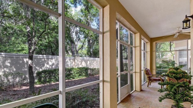 Une terrasse couverte avec de grandes fenêtres, un ventilateur de plafond et une vue sur un jardin aménagé.