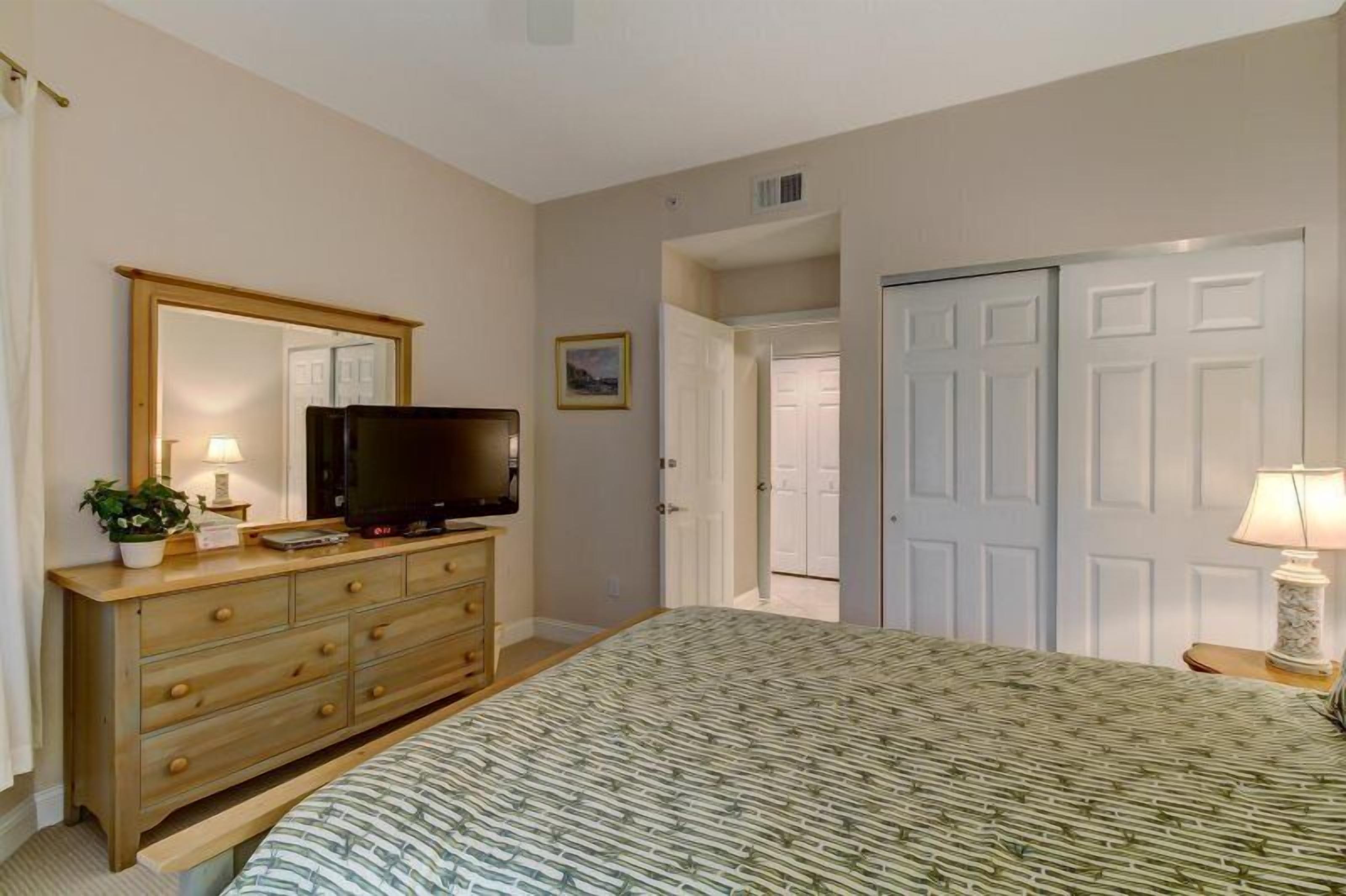 Een slaapkamer met een bed, een kaptafel, een televisie en een deur naar een andere kamer.