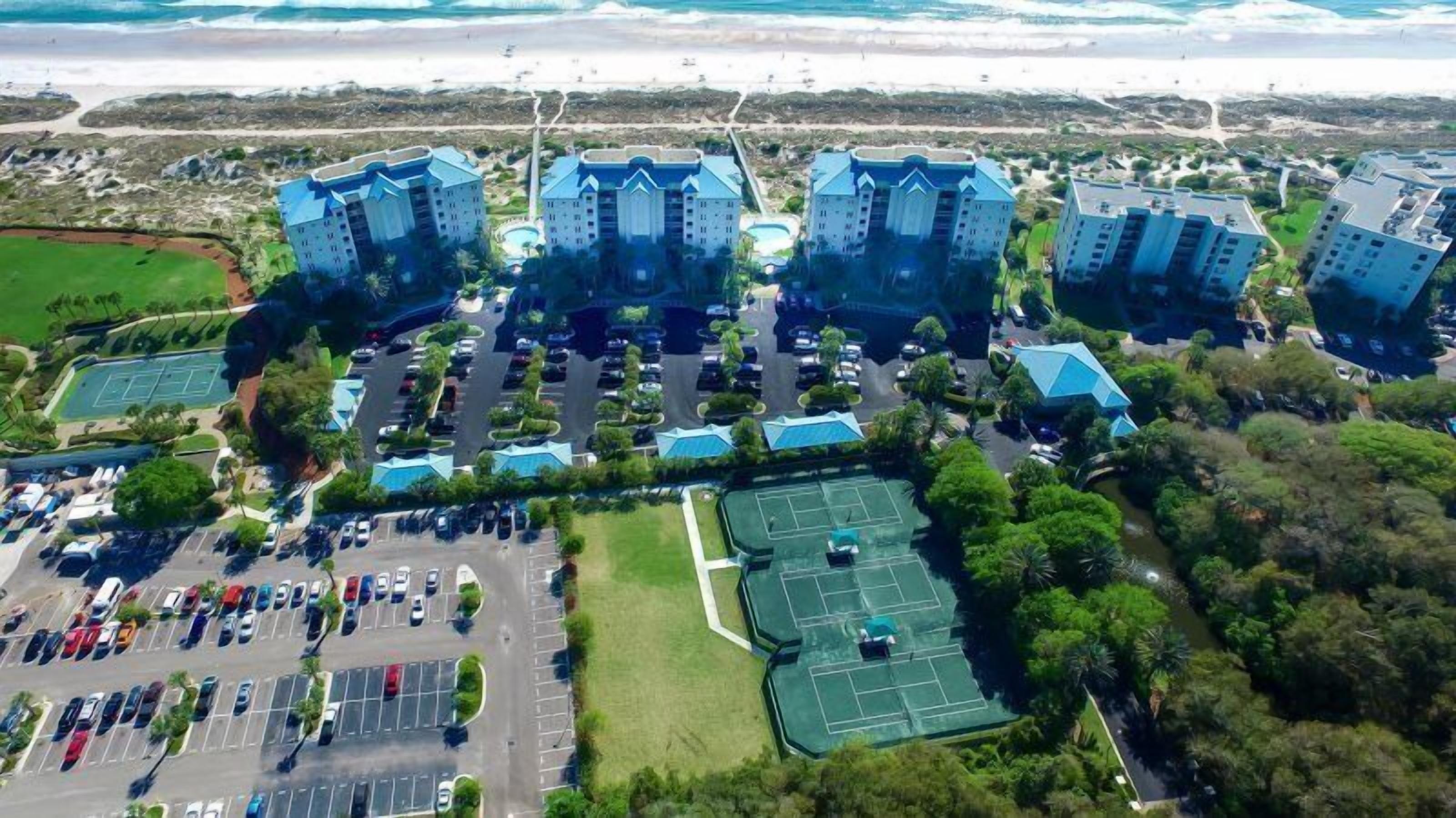 A large hotel complex with multiple blue-roofed buildings, a central courtyard, and a parking lot.