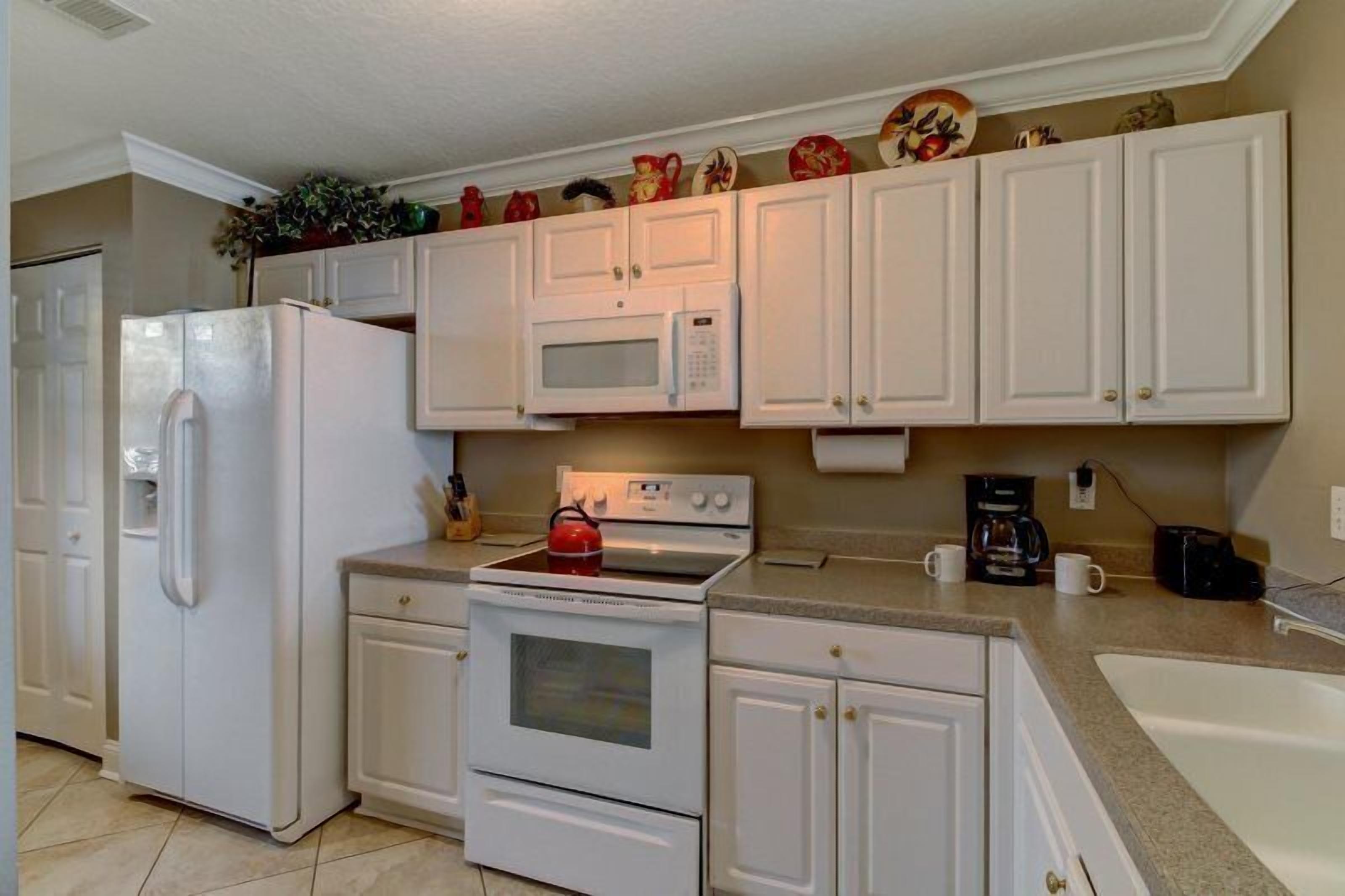 A kitchen with white cabinets, a refrigerator, a microwave, an oven, and a coffee maker.