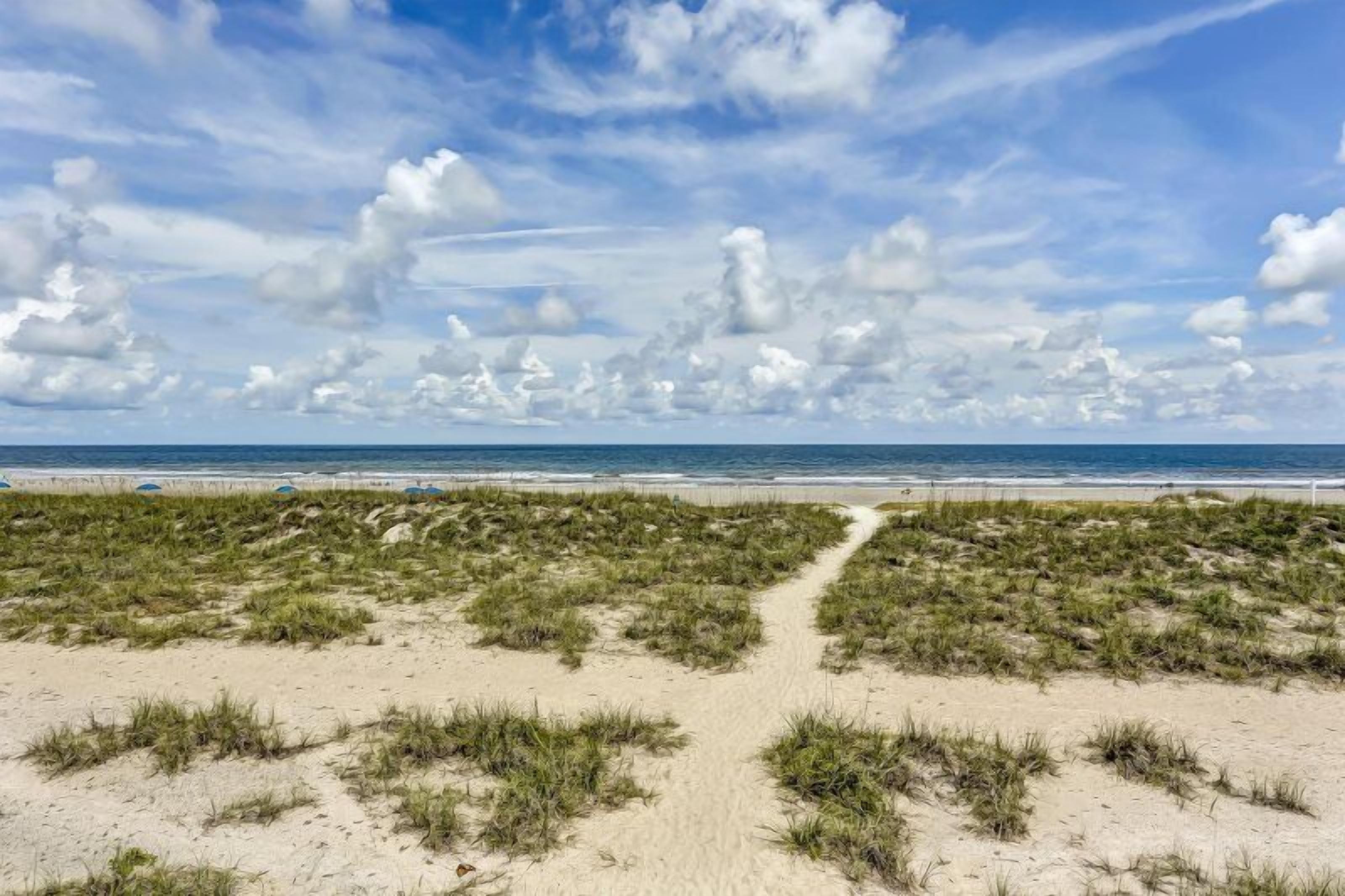 A beach with a sandy path leading to the ocean, under a partly cloudy sky.