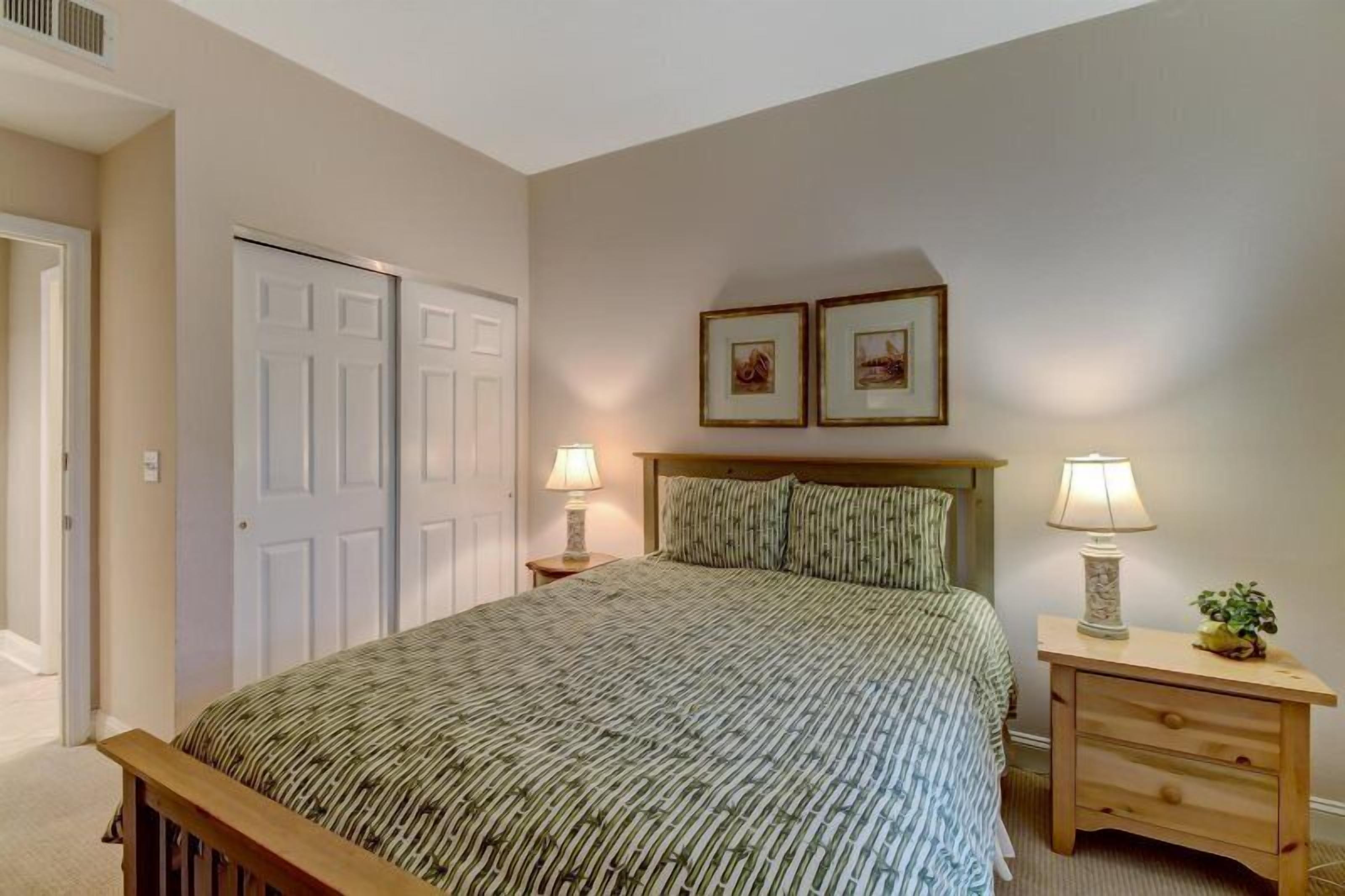 A bedroom with a bed, two bedside tables with lamps, a headboard, and two framed pictures on the wall.