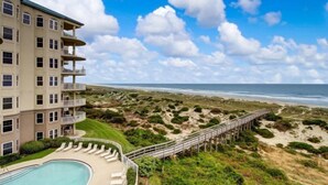 Un hotel frente a la playa con piscina, una pasarela de madera y vista al océano.