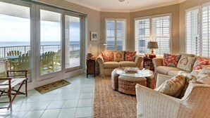 A spacious living room with a large sliding glass door leading to a balcony, a ceiling fan, and a view of the ocean.