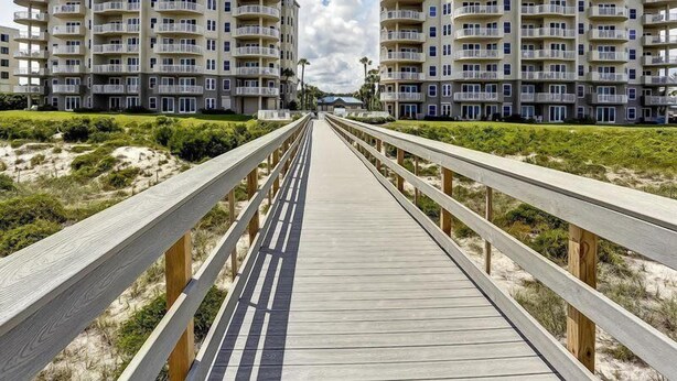 A wooden boardwalk leading to beachfront apartments with balconies and a clear sky.