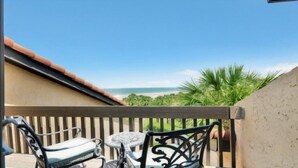 Ein Balkon mit Blick auf den Strand, ein Stuhl und ein kleiner Tisch.