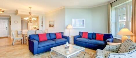 Un salon avec deux canapés bleus, un fauteuil à motifs, une table basse et un ventilateur de plafond.