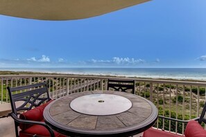 A round table with a white center, surrounded by chairs with red cushions, on a balcony overlooking a beach with a clear sky. - 82-ocean-place (Fernandina Beach)
