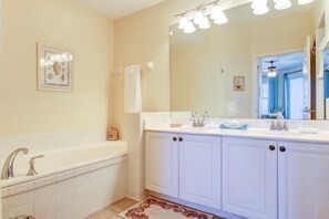 A bathroom with a bathtub, a large mirror, and white cabinetry. - 82-ocean-place (Fernandina Beach)