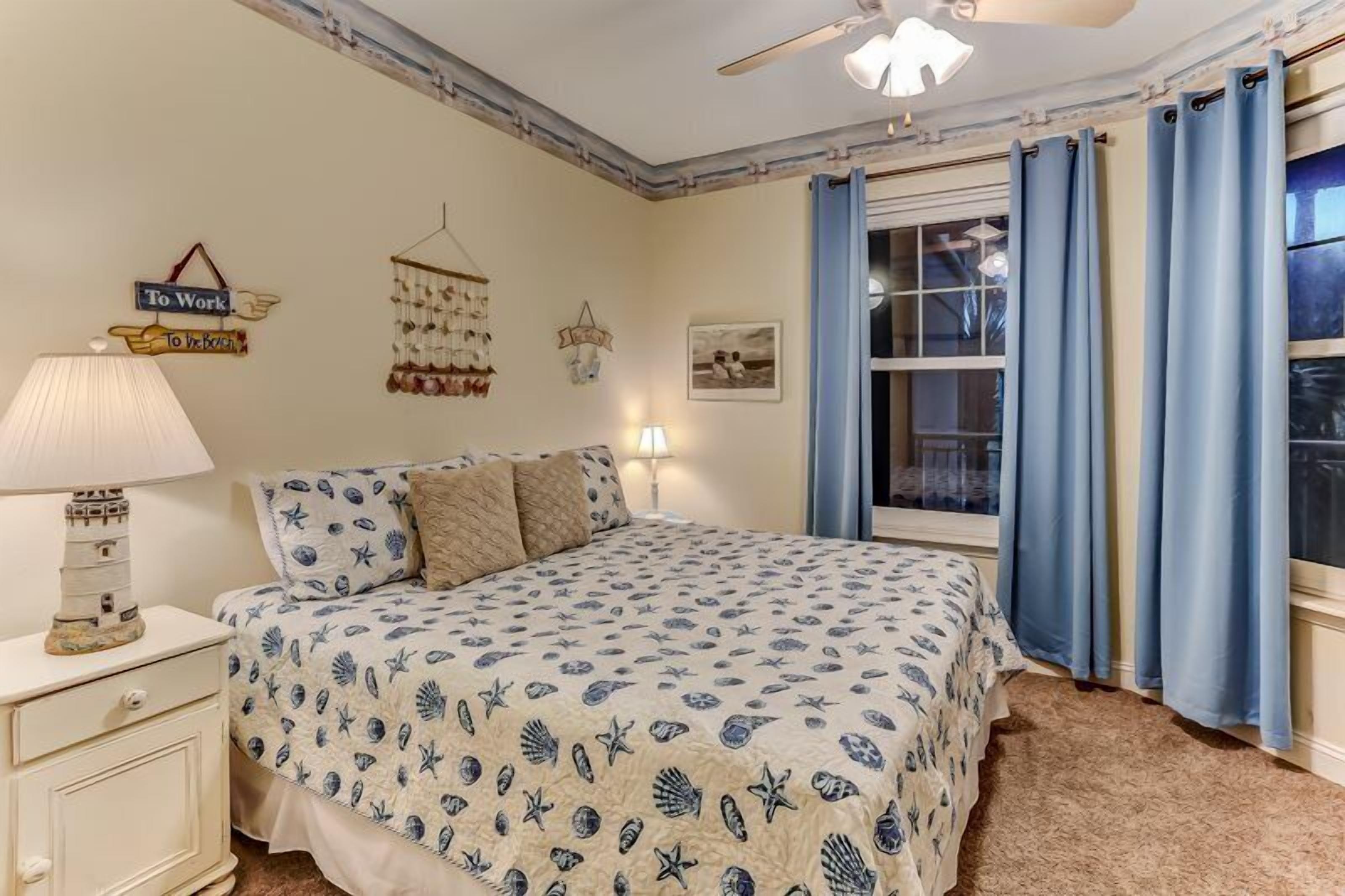 Une chambre à coucher comprenant un lit, une table de chevet, une lampe, une fenêtre avec des rideaux et des éléments de décoration murale.