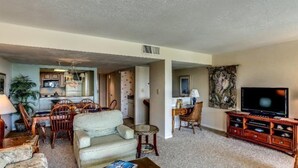 A living room with a sofa, chairs, a coffee table, a TV, and a kitchen area in the background. - 1340-shipwatch (Fernandina Beach)
