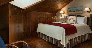 A bedroom with a wooden ceiling, a bed with striped bedding, a red throw, and two wall-mounted lamps. - Katies-light (Fernandina Beach)