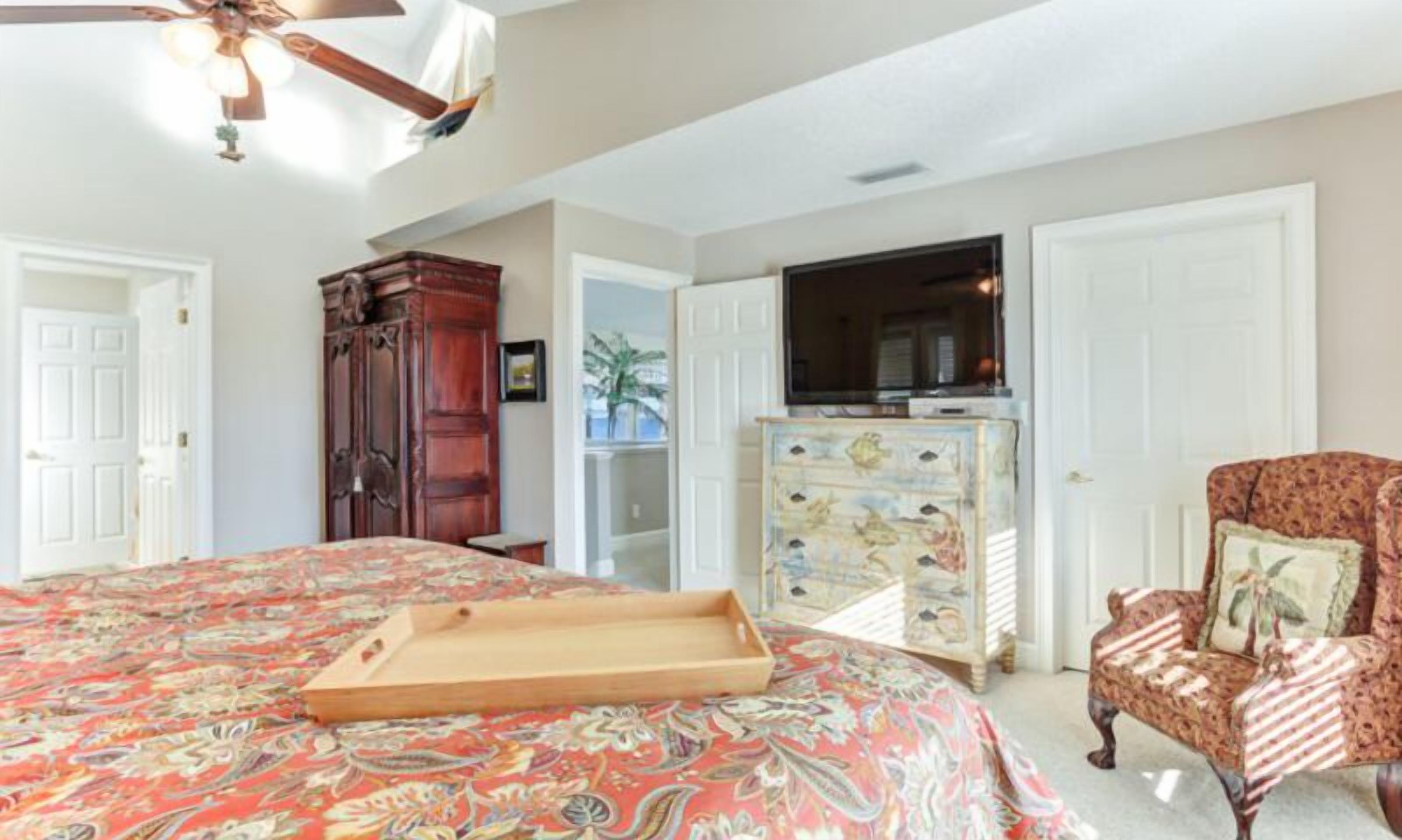 A bedroom with a large bed, a wooden dresser, a television, and a chair.