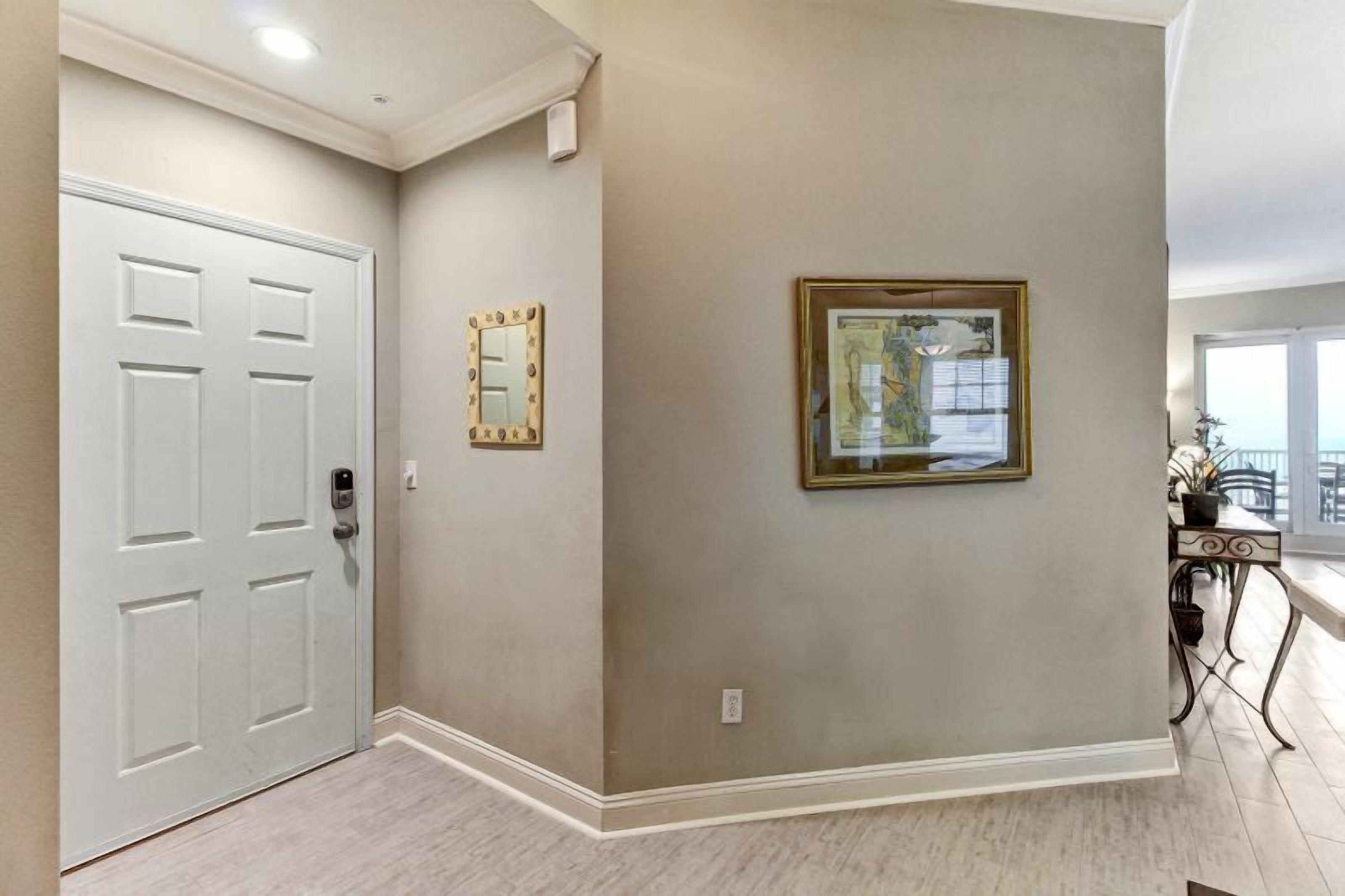 A hallway with a white door, a framed mirror, and a framed artwork on the wall.