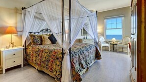 A four-poster canopy bed with a floral bedspread, bedside tables with lamps, a view of the sea through a window, and a seating area with chairs. - 25-ocean Place (Fernandina Beach)