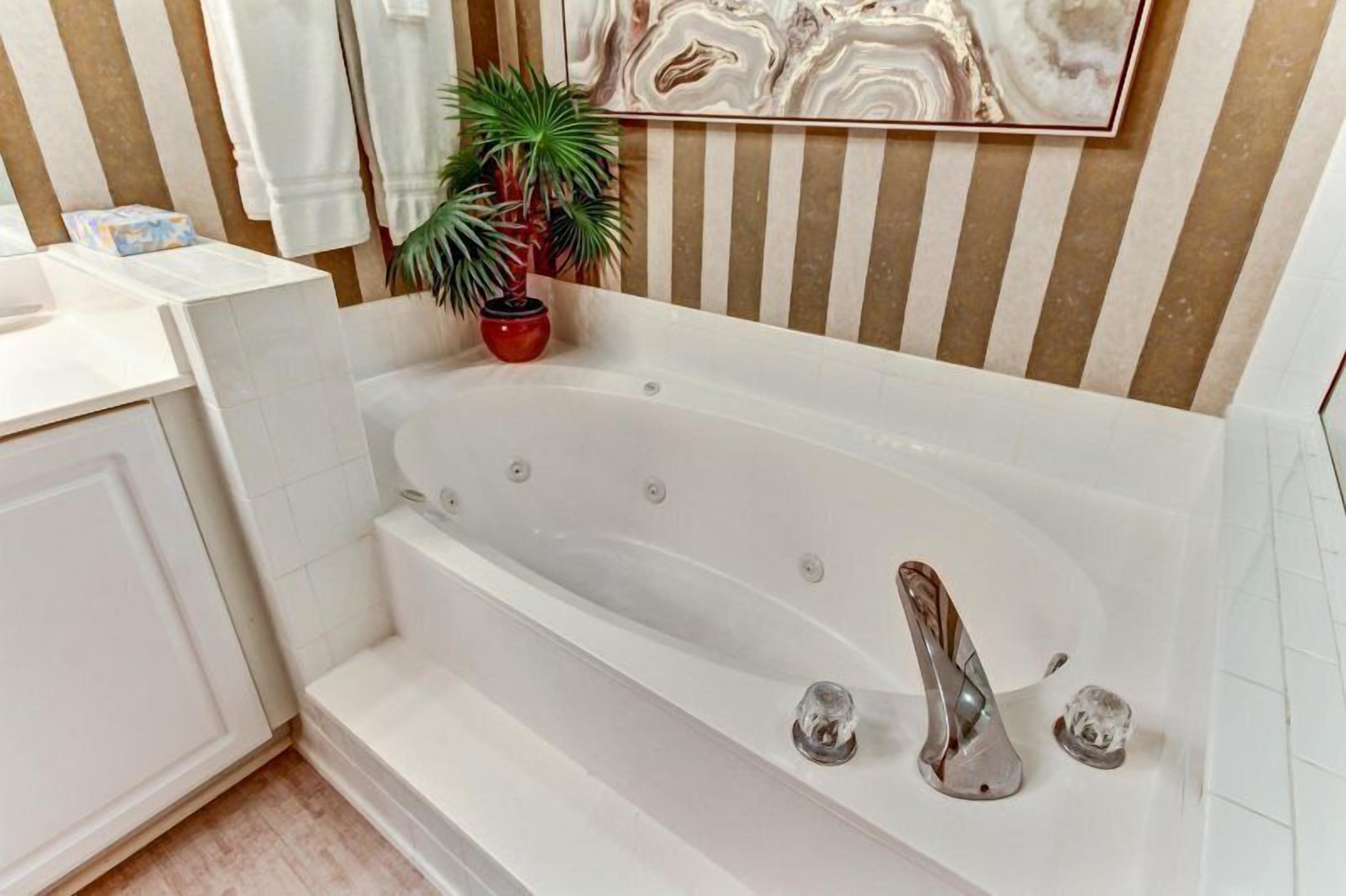 A modern bathroom with a freestanding bathtub, a potted plant, and striped wall decor.