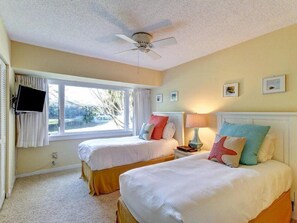 A bedroom with two beds, a ceiling fan, a TV, and a window with curtains.