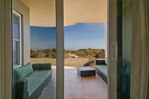 A room with a view of a beach and dunes, featuring a sofa and a small table.