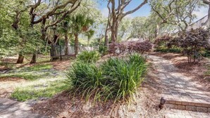 A landscaped garden with a paved pathway, various shrubs, and mature trees. - 503-sailmaker (Fernandina Beach)