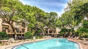 A swimming pool surrounded by trees and lounge chairs, with a building in the background. - 503-sailmaker (Fernandina Beach)