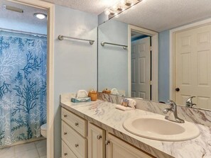 A bathroom with a marble sink, a mirror, and a shower curtain with a tree pattern. - 503-sailmaker (Fernandina Beach)