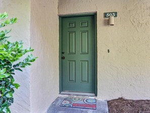 A green door with a number plate '503' above it, a welcome mat with a colorful design, and a plant to the left. - 503-sailmaker (Fernandina Beach)
