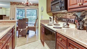 A kitchen with wooden cabinets, a microwave, a stove, and a dining area with a chair. - 503-sailmaker (Fernandina Beach)