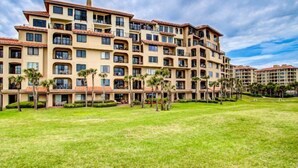 A multi-story hotel with balconies, a well-maintained lawn, and palm trees. - 1830-turtle-dunes (Fernandina Beach)
