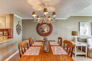 A dining area with a wooden table, chairs, a chandelier, a decorative mirror, and a sofa in the background. - C123-amelia-surf-and-racquet - 1303311 (Fernandina Beach)