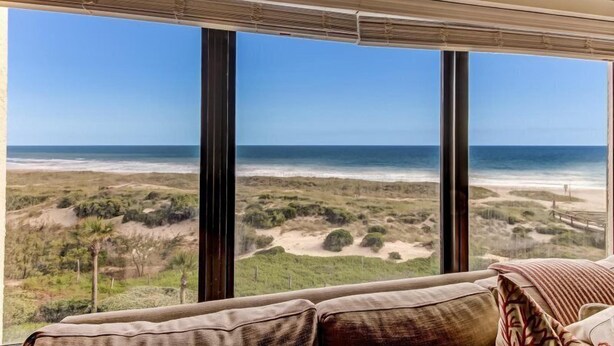 Una habitación con amplios ventanales con vistas a una playa y dunas.