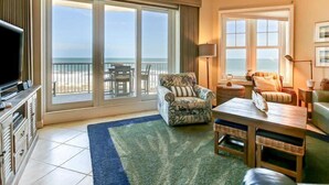 Ein geräumiges Wohnzimmer mit einer großen Schiebeglastür, die auf einen Balkon mit Blick auf den Strand führt.