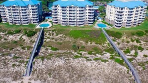 Ein Hochhaus-Hotel mit mehreren Balkonen, einem zentral gelegenen Pool und einer Brücke zum Strand.