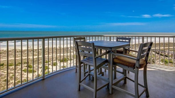 Ein Balkon mit Tisch und Stühlen mit Blick auf einen Strand.