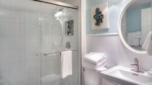 A modern bathroom with a glass shower enclosure, a white sink, and a large mirror. - 1141 Beachwalker (Fernandina Beach)