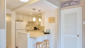A compact kitchen with a central island, pendant lighting, and a sign indicating the direction to the beach. - 1141 Beachwalker (Fernandina Beach)