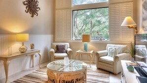 A cozy living room with a large window, wicker furniture, and a lamp. - 1141 Beachwalker (Fernandina Beach)