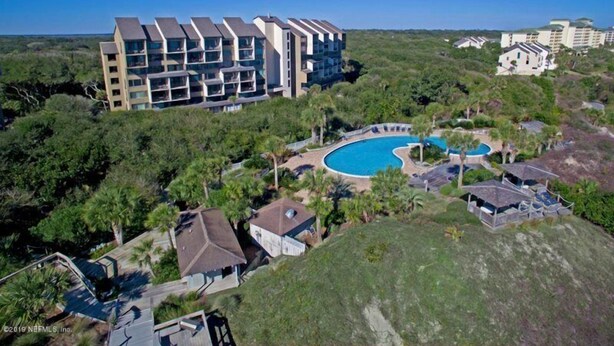 A modern hotel with multiple balconies, a central swimming pool, and lush greenery surrounding the property. - 1141 Beachwalker (Fernandina Beach)