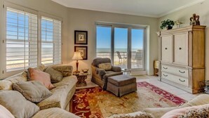 A spacious living room with a large window, a ceiling fan, and a wooden cabinet. - 57-ocean-place (Fernandina Beach)