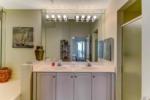 A bathroom with a double sink vanity, a large mirror, and a ship painting on the wall.