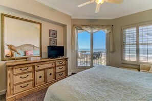 A bedroom with a large bed, a dresser, a TV, and a balcony with a view of the ocean.